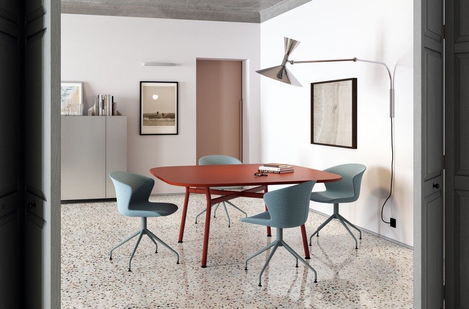 Quatre chaises de réunion KICCA PLUS bleu avec piètement pivotant assorti, disposées autour d'une table design rouge brique dans un intérieur épuré.