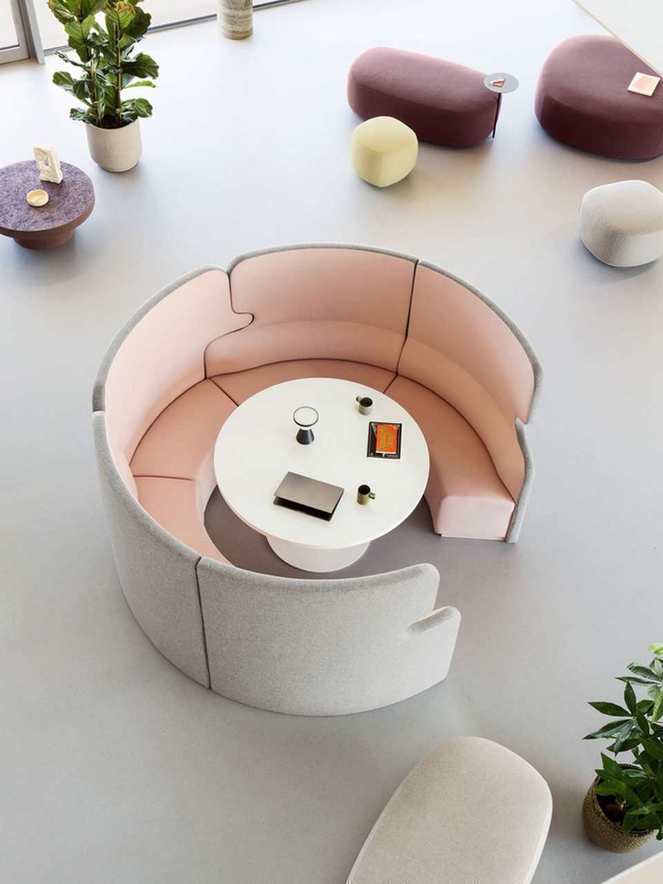 Vue en plongée de l'alcôve acoustique circulaire TALK en tissu gris et rose au sein d'un grand espace lounge d'entreprise, entourée de poufs modulaires et de plantes de bureau.
