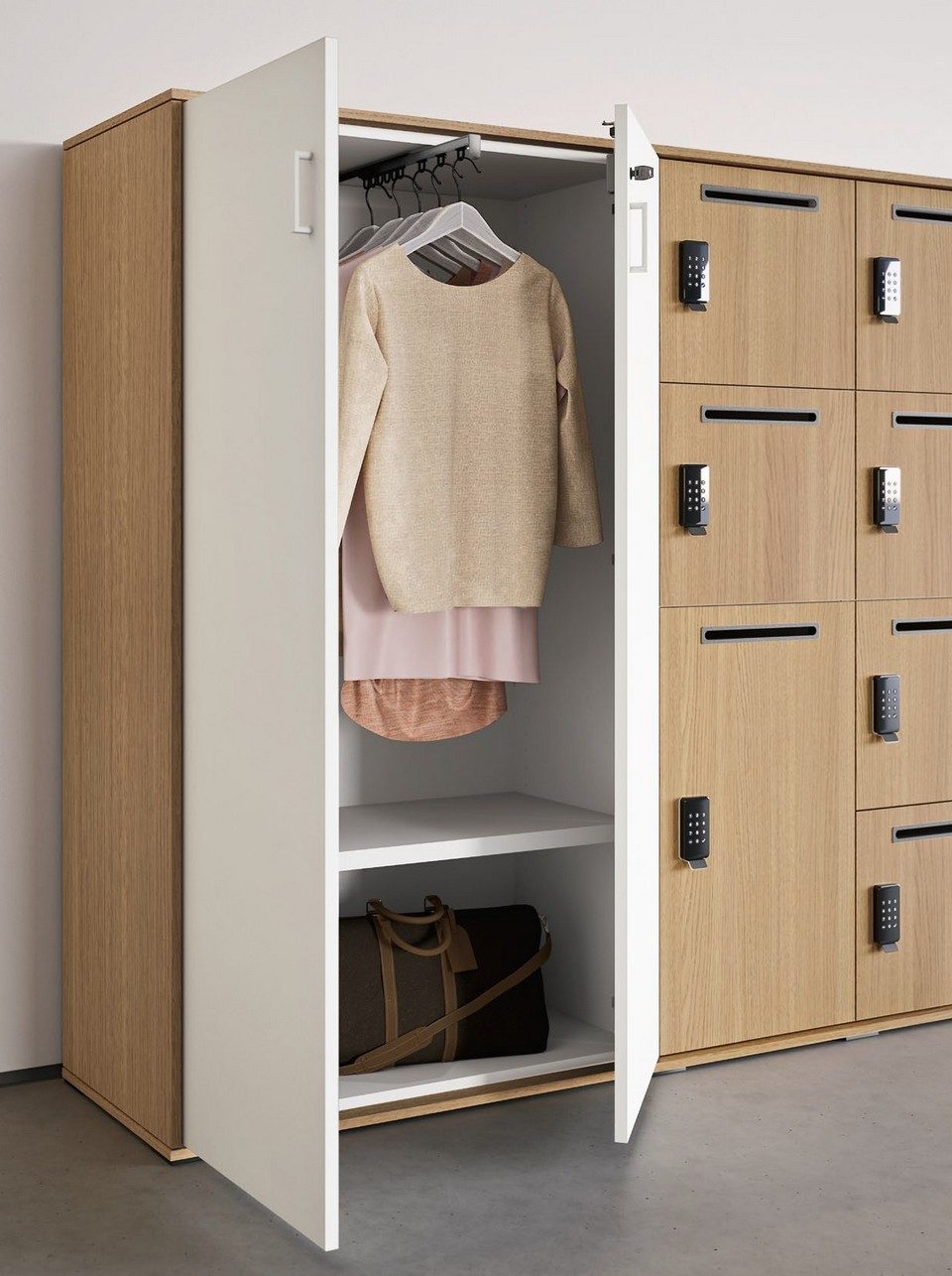 Zoom sur une penderie ouverte intégrée à l'armoire casier personnalisable GALAXY, révélant des vêtements suspendus et un sac de voyage en cuir marron. Sur la droite, l'alignement de casiers de bureau en bois clair est équipé de fentes à courrier individuelles et de serrures à code électroniques noires pour l'aménagement d'un flex-office sécurisé.