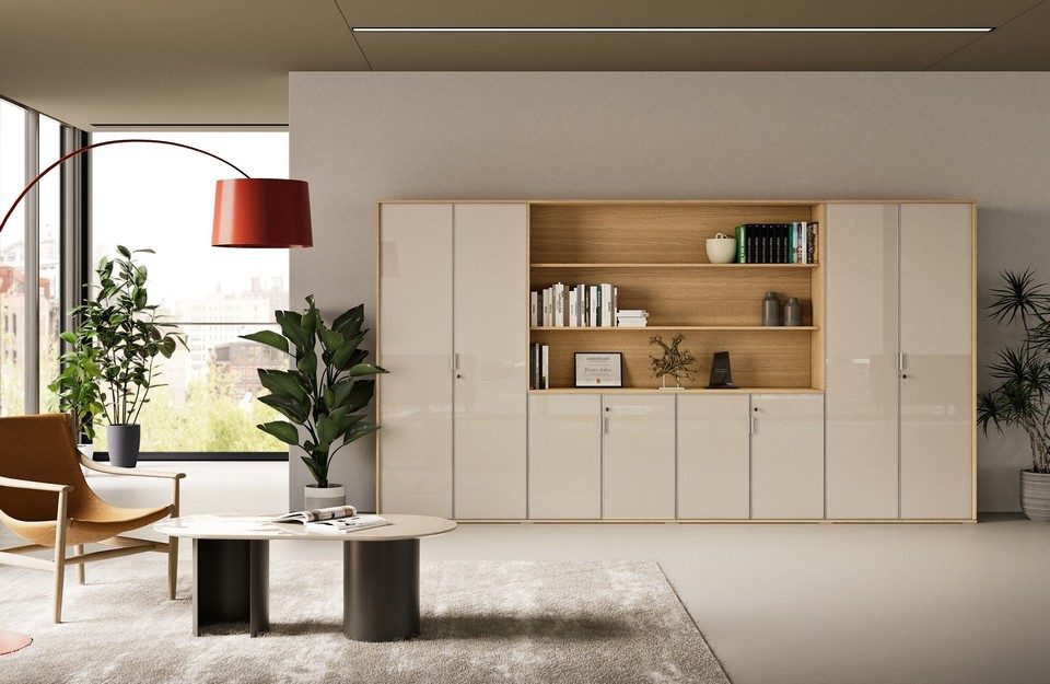 Vue de face de l'armoire de bureau personnalisable GALAXY combinant de grands placards de rangement en finition verre laqué beige brillant et une grande niche centrale ouverte en chêne clair faisant office de bibliothèque décorative, installée dans un espace lounge professionnel chaleureux et moderne.