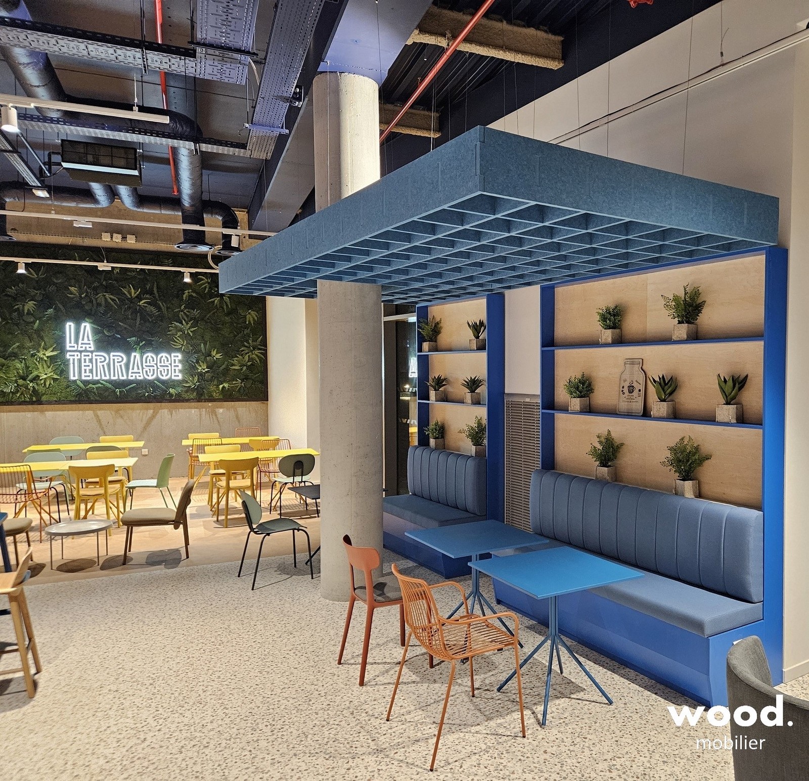 Baffle acoustique suspendue en PET bleu au-dessus d'un espace de restauration d'entreprise avec banquette intégrée.