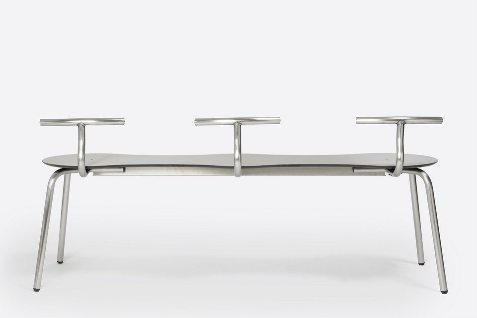 Banc extérieur à 3 places en acier inoxydable avec trois dossiers tubulaires amovibles TAM par Ondarreta. Longue assise ondulée gris foncé et structure en inox brossé au design minimaliste pour amencement de terrasse de restaurant, hôtel et espace bistrot moderne.
