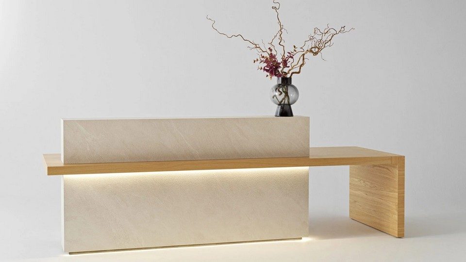 Banque d'accueil monolithique KYO en finition minérale beige clair BioArgile avec éclairage LED continu intégré sous le plateau en bois et au socle. Le meuble présente une configuration avec extension en aile libre pour l'accessibilité.