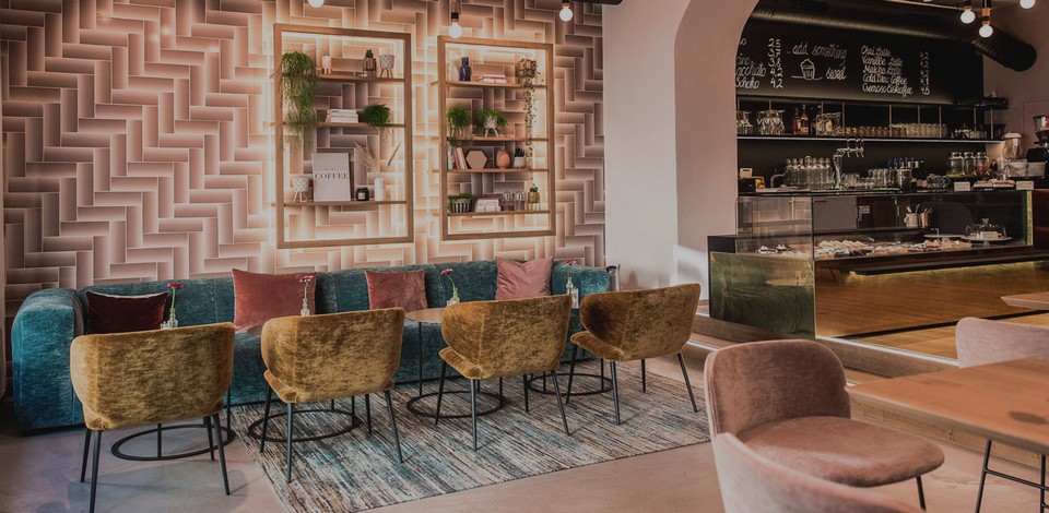 Banquette de restaurant sur mesure ADRENALINE en velours bleu sarcelle, intégrée dans une zone café lounge avec fauteuils et décor mural lumineux.