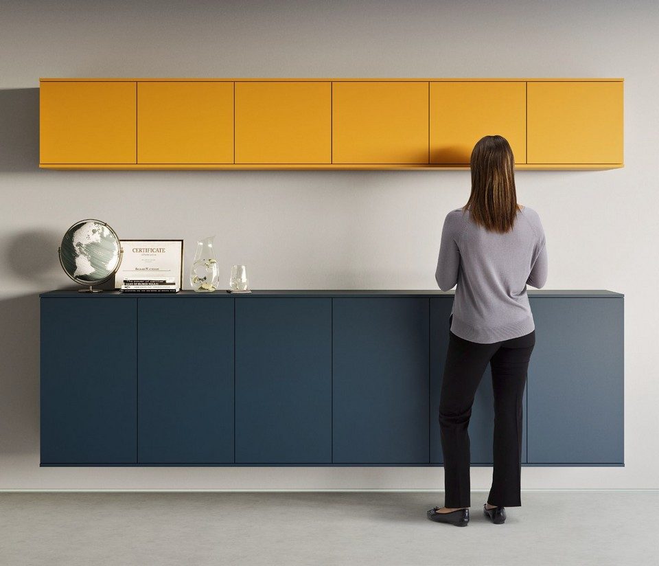 Vue d'ensemble du système de buffet suspendu et d'armoires murales modulaires GALAXY de couleur bleu marine et jaune moutarde. Fixé directement au mur sans piètement au sol, cet ensemble de rangement épuré sans poignées apparentes (ouverture push-pull) structure l'espace tout en facilitant l'entretien des sols.