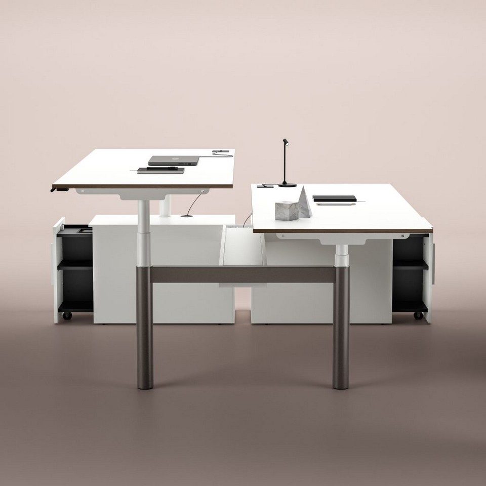 Bureau bench assis-debout double blanc NUVOLA de Bralco avec postes de travail réglables en hauteur de manière indépendante, mis en scène avec des meubles de rangement de service intégrés sous le plateau.