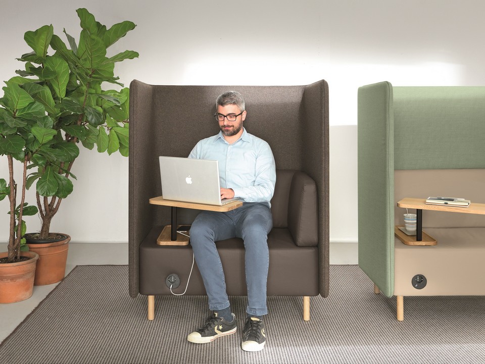 Gros plan d'un collaborateur travaillant sur ordinateur dans un fauteuil NUCLEO avec tablette bois.