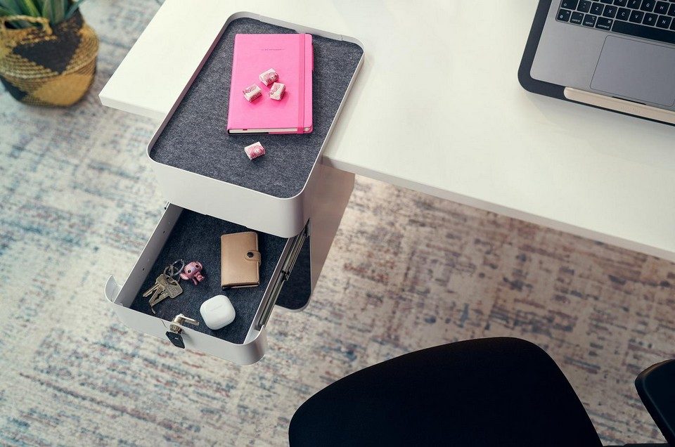 Vue de dessus d'un caisson de bureau suspendu BENTO blanc avec son tiroir à clé ouvert contenant des clés et des écouteurs, fixé sur un plan de travail blanc équipé d'un tapis supérieur en feutre gris.