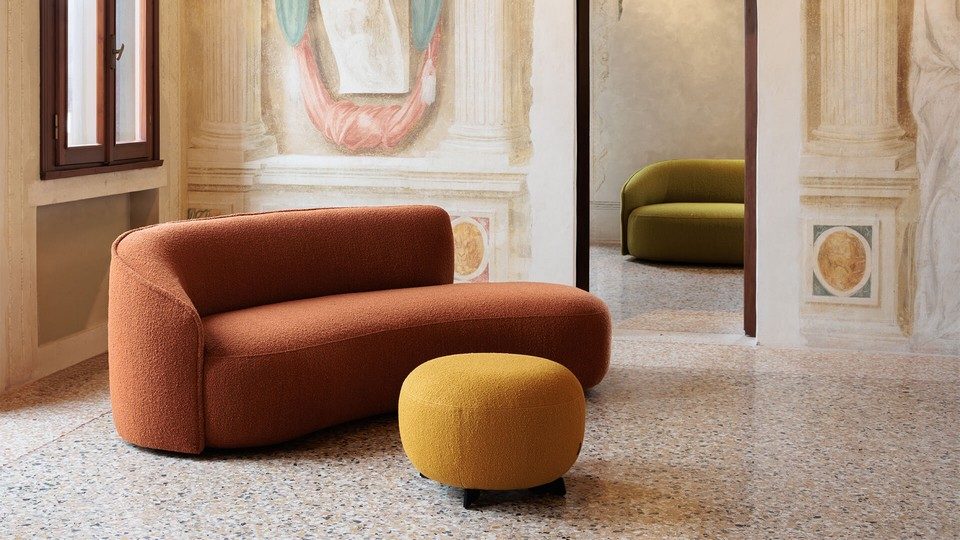 Canapé d'attente organique SIBILLINO en tissu terracotta, agencé avec un pouf rond moutarde dans un hall de réception haut de gamme aux murs ornés de fresques. Un second canapé lounge vert olive est visible en arrière-plan.