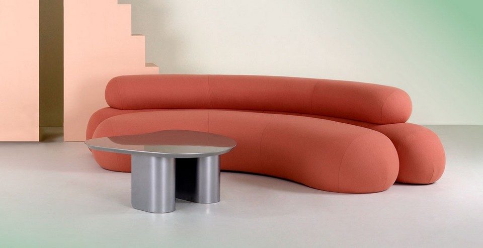 Canapé lounge ADRENALINE sur mesure, en tissu corail, forme organique et arrondi, présenté avec une table basse design pour les espaces d'accueil.