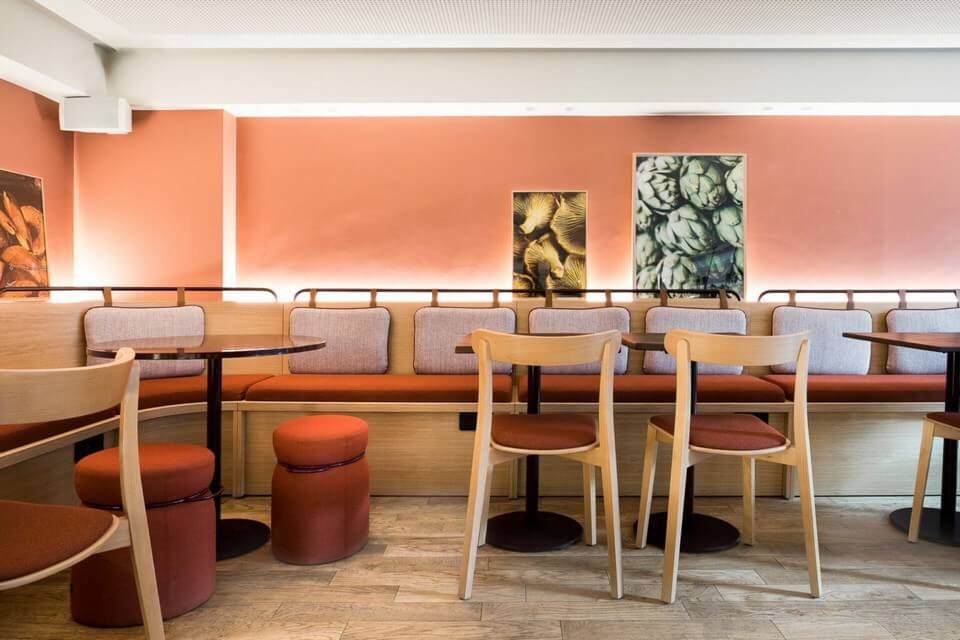 Chaise de restaurant ICHO en bois clair avec assise en tissu orange, dans un aménagement de café contemporain aux murs couleur pêche, soulignant l'intégration design.