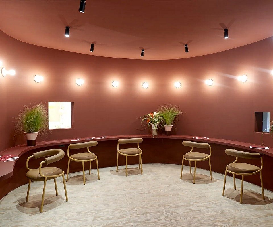 Aménagement circulaire avec cinq chaises KOALA OPEN à dossier ajouré boudin moutarde devant un comptoir filant rouge brique