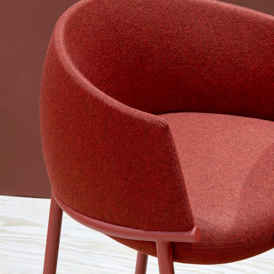Gros plan sur l'assise et le dossier enveloppant en tissu rouge chiné de la chaise KOALA avec structure en acier coordonnée