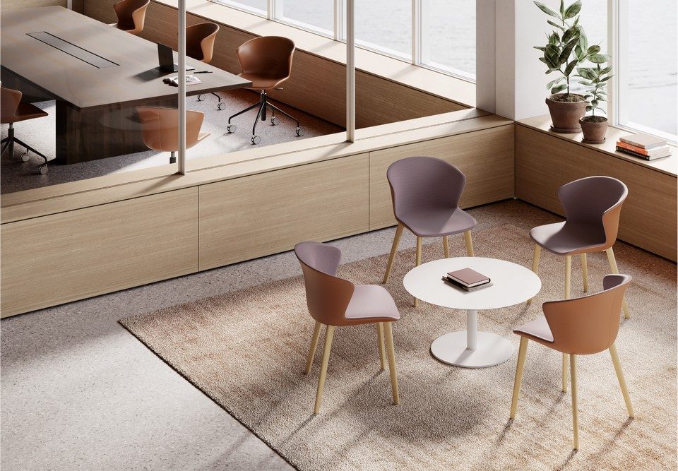 Aménagement d'un coin détente avec quatre chaises KICCA PLUS bicolores (intérieur mauve, extérieur terre cuite) sur piètements en bois d'érable, autour d'une table basse ronde, et des chaises pivotantes en cuir en arrière plan.