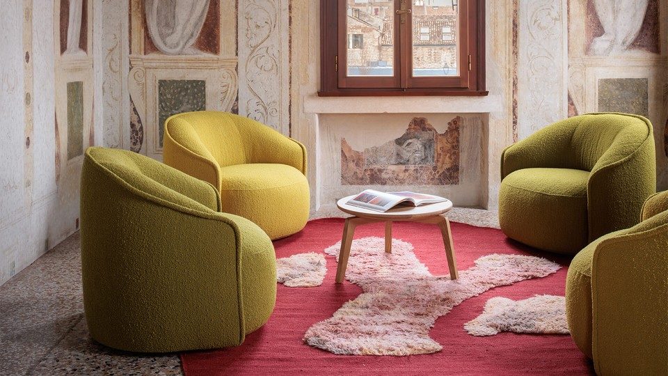 Quatre fauteuils lounge professionnels SIBILLINO en tissu bouclé jaune moutarde et vert olive, disposés autour d'une table basse en bois sur un tapis rouge dans une zone d'attente premium.