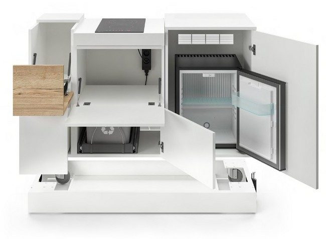 Kitchenette mobile MAG blanche avec portes et abattants ouverts révélant ses équipements techniques intégrés : plaque de cuisson à induction, mini-réfrigérateur, bac de tri sélectif et bloc de prises électriques. Vue de face illustrant l'optimisation intérieure de cette cuisine de bureau compacte sur roulettes pour l'aménagement des espaces de pause en entreprise.