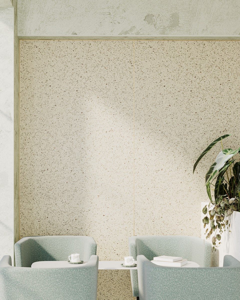 Habillage acoustique mural imprimé effet terrazzo beige avec inserts dorés en laiton, installé dans un espace d'accueil ou de coworking premium composé de fauteuils lounge vert pastel. Solution écoresponsable d'insonorisation et de correction sonore haut de gamme pour l'architecture tertiaire et hôtelière.