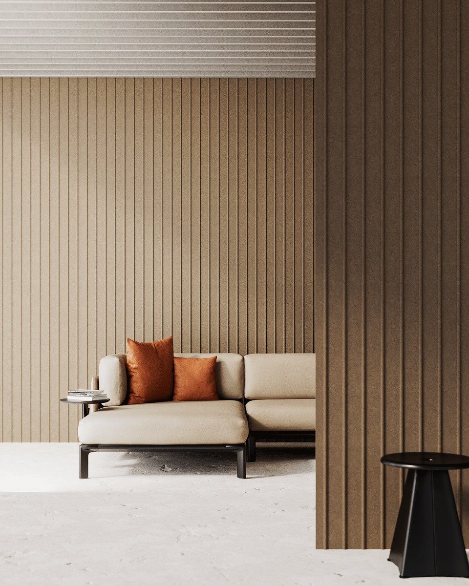 Grand habillage acoustique mural tridimensionnel marron beige aux lignes verticales régulières installé dans un salon professionnel avec canapé moderne et coussins terre cuite. Revêtement phonique en feutre pour la correction acoustique et la décoration design d'espaces lounge ou de bureaux tertiaires.