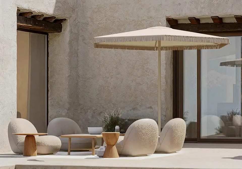 Espace lounge extérieur d'un établissement haut de gamme avec parasol NATA à franges et assises organiques.