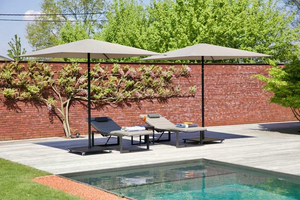 Paire de parasols NATA à mât central ombrageant des bains de soleil sur une terrasse de piscine contemporaine.