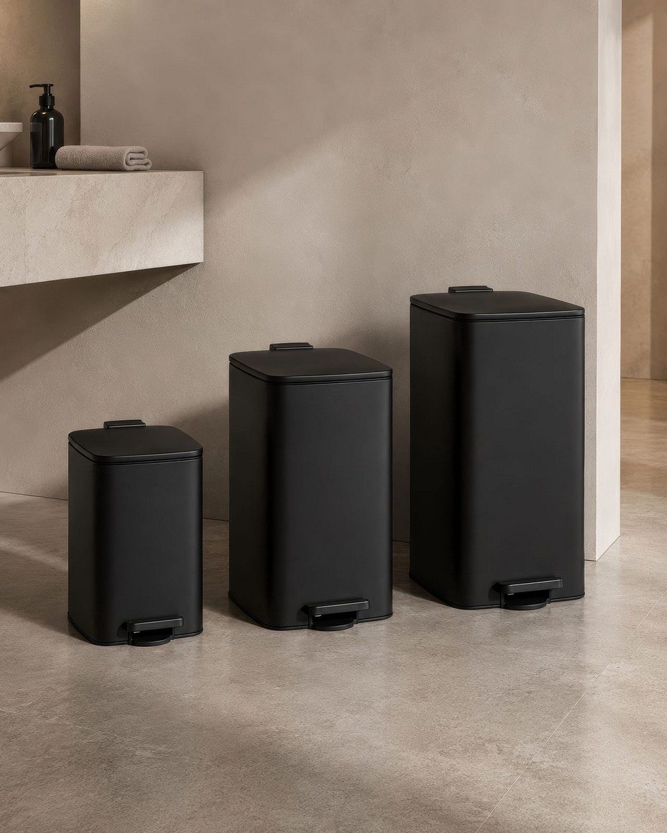 Trois poubelles à pédale noires mates de tailles différentes alignées dans une salle de bain d'hôtel moderne. Solution de gestion des déchets discrète et hygiénique pour sanitaires professionnels.