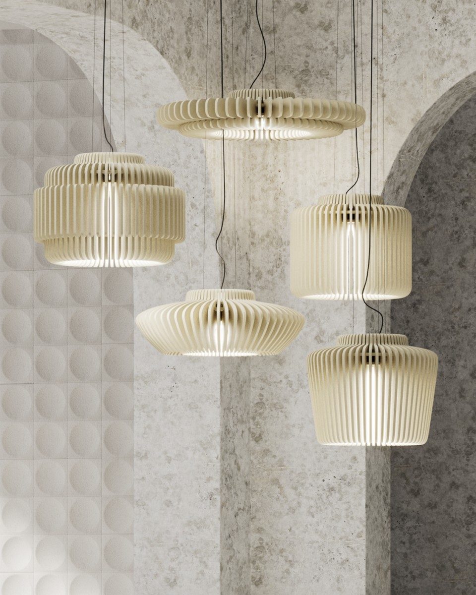 Une grappe de suspensions d'éclairage acoustique design RAYA installée en cascade sous des voûtes architecturales en pierre brute. Les luminaires révèlent différentes formes géométriques de diffuseurs composés de lamelles verticales en feutre de PET recyclé beige, alliant correction sonore haute performance et éclairage LED pour les bureaux tertiaires premium.