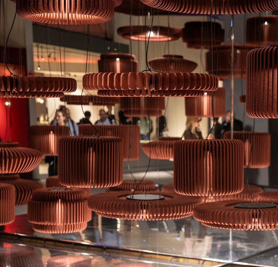 Installation dense en cascade de suspensions d'éclairage acoustique RAYA en feutre de PET recyclé coloris terracotta. Luminaires phoniques design en lamelles verticales rayonnantes pour la correction acoustique et l'aménagement lumineux architectural de grands espaces professionnels.
