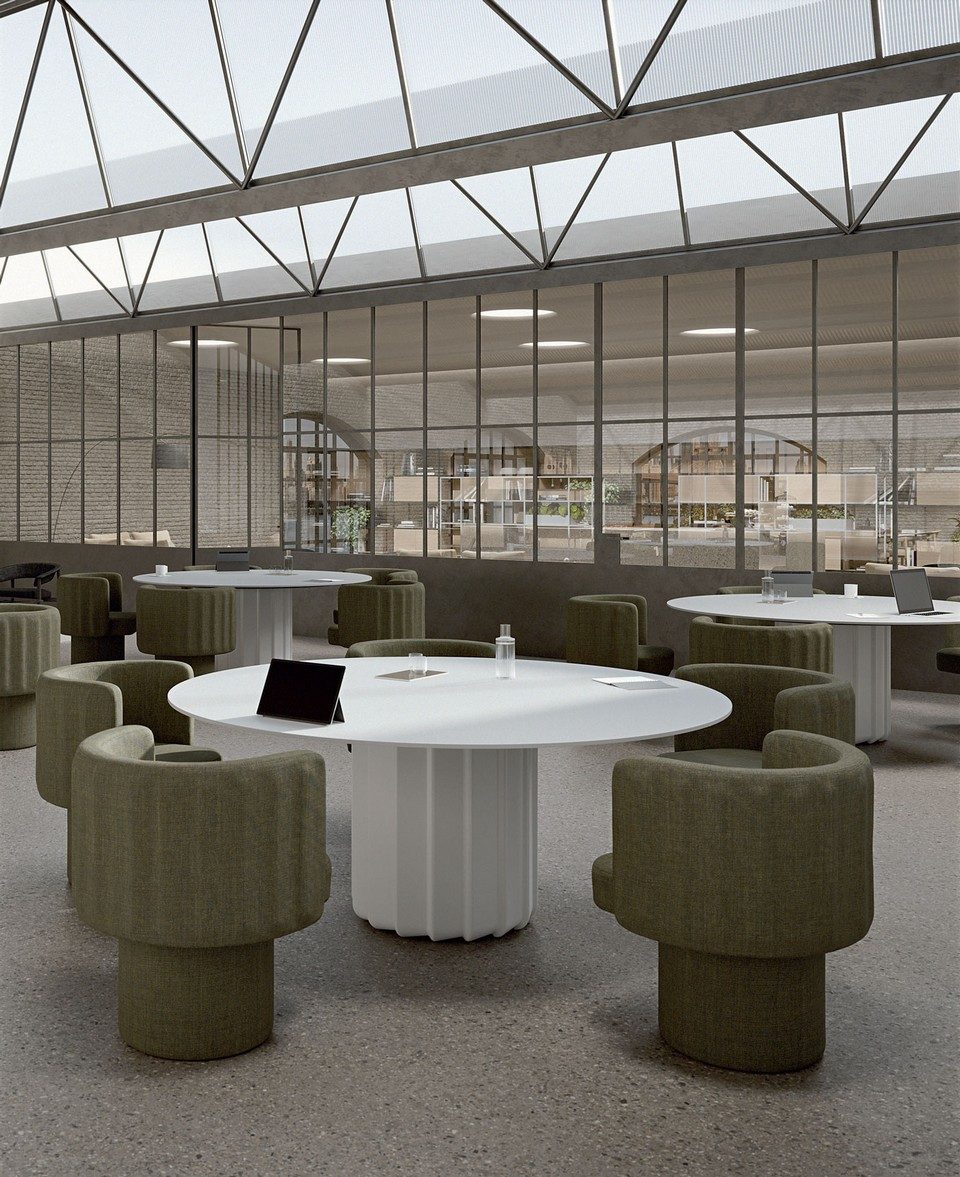 Tables de réunion rondes blanches SABREE à colonne centrale flûtée et fauteuils lounge vert olive dans un grand espace de coworking de style industriel avec verrière.