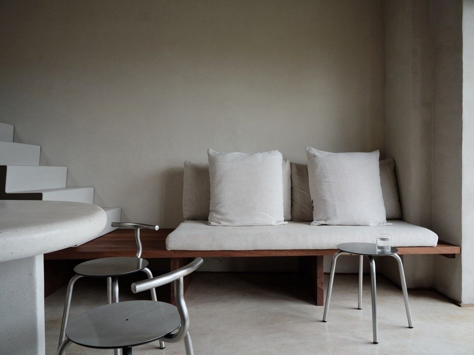Quatre tabourets bas H45 en acier inoxydable avec et sans dossier amovible TAM par Ondarreta disposés autour d'une table ronde blanche. Mobilier de terrasse en inox au design minimaliste et tendance chrome pour agencement de restaurant style bistrot moderne.