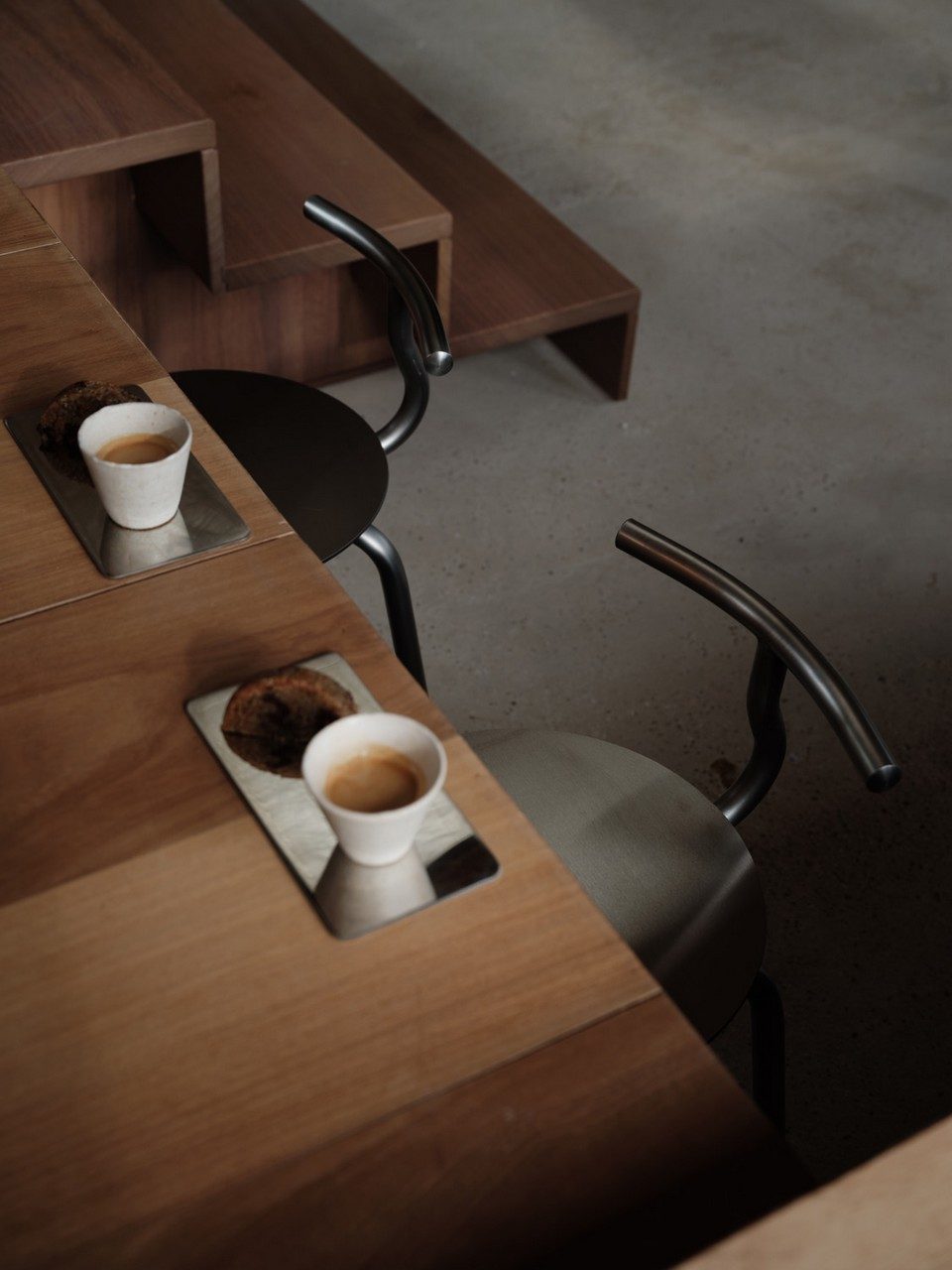 Vue plongeante de deux tabourets de bar en acier inoxydable brossé avec dossier TAM près d'une table en bois de café restaurant. Mobilier extérieur au design tubulaire minimaliste et tendance chrome pour agencement de terrasse style bistrot moderne.